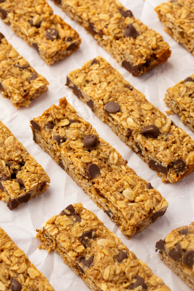 Rows of homemade gluten-free granola bars with gluten-free oats and chocolate chips are arranged on crinkled white parchment paper. The bars are rectangular and appear chewy with visible chocolate pieces.
