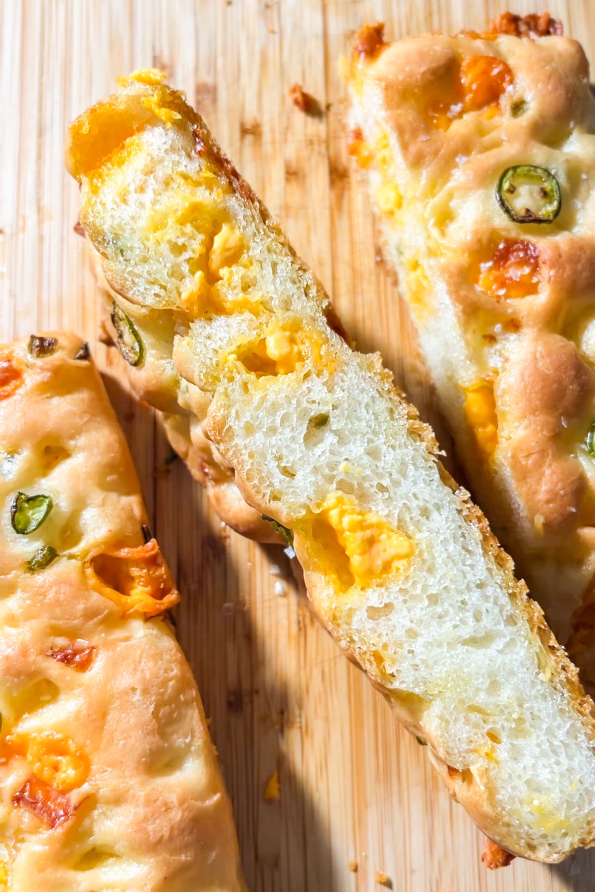 Sliced focaccia bread on a wooden surface, topped with melted cheese and jalapeño slices. The bread looks soft and airy with a golden crust.