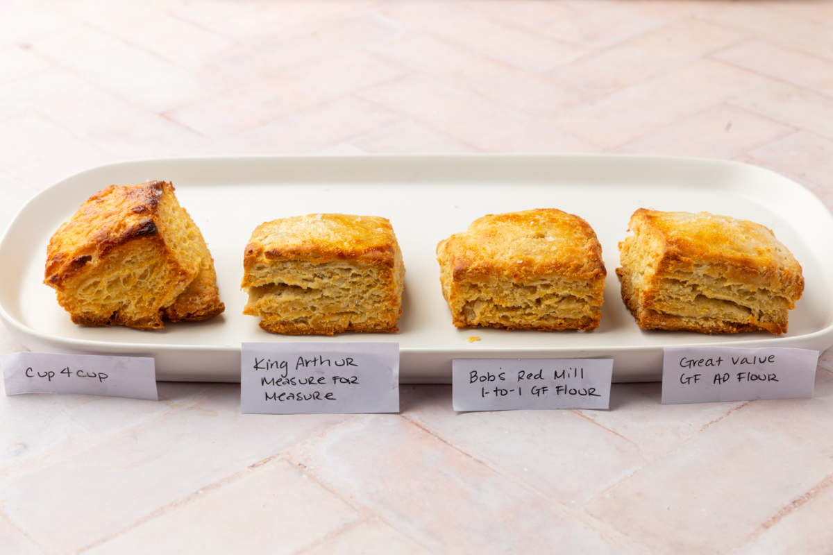 Four square biscuits are lined up on a white tray, each labeled with a different gluten-free flour brand: Cup 4 Cup, King Arthur Measure for Measure, Bob’s Red Mill 1-to-1 GF Flour, and Great Value GF AP Flour.