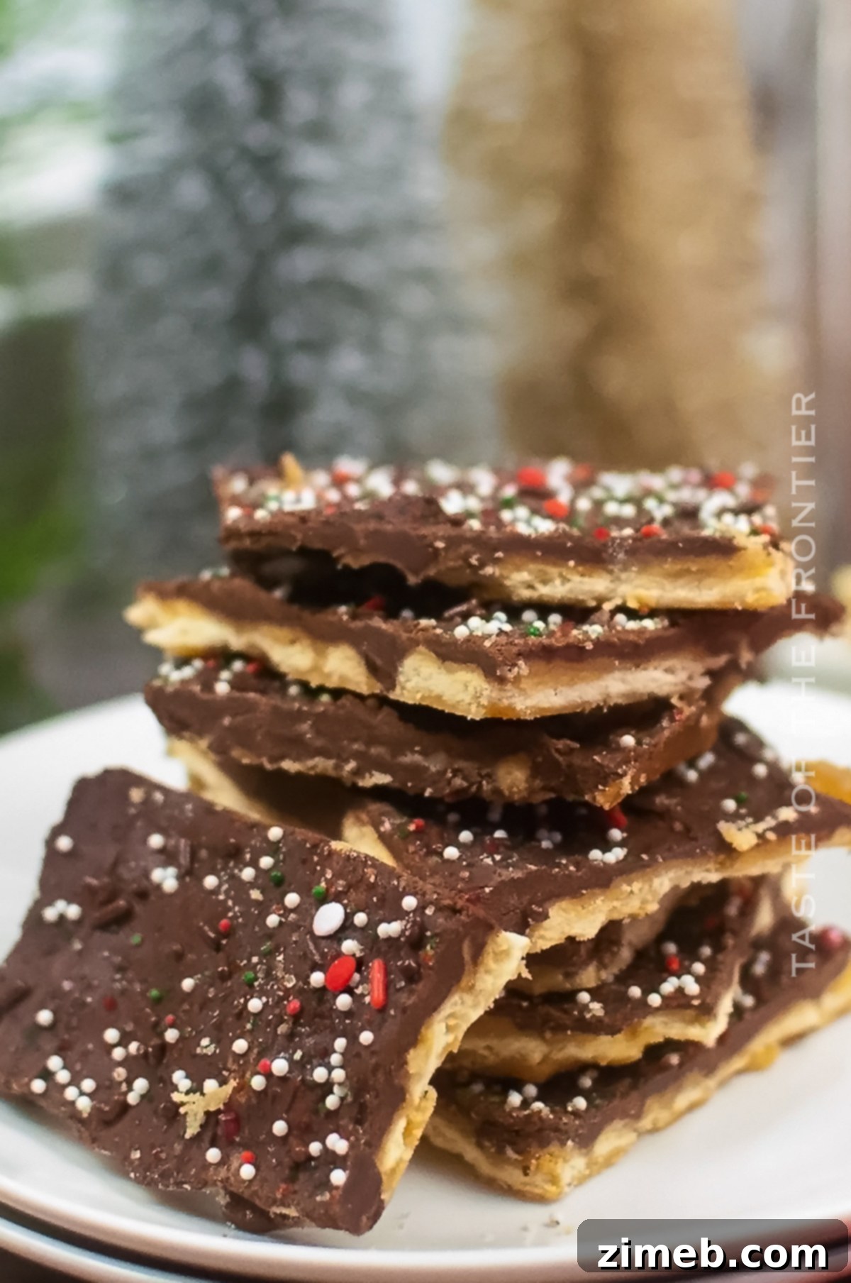 Yuletide Toffee Bliss 15 A festive close-up of Christmas Crack pieces arranged on a white platter, showcasing the melted chocolate and colorful sprinkles over the toffee and cracker base.