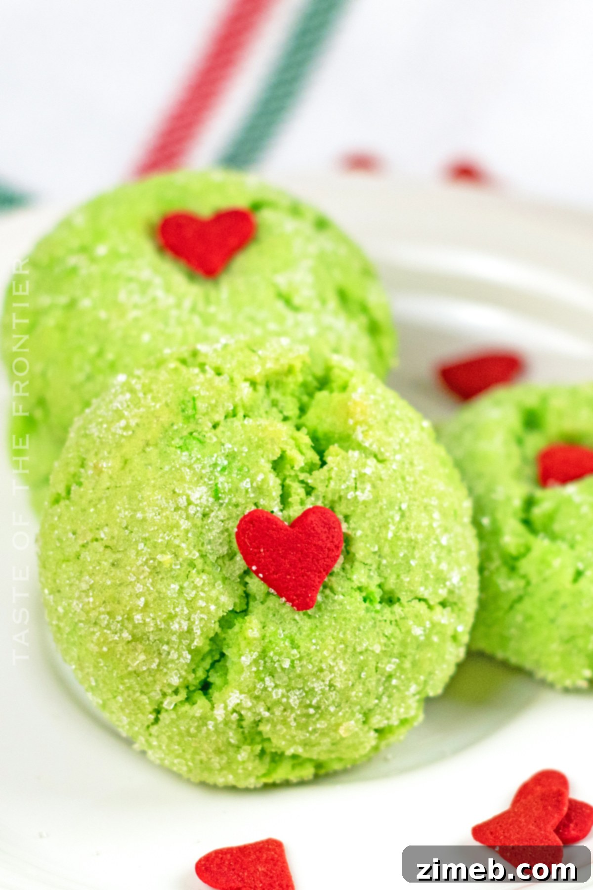 Grinch's Heart-Melting Crinkles 2 Soft and chewy Grinch crinkle cookies with a bright green color and a small red heart on top, arranged festively for Christmas.