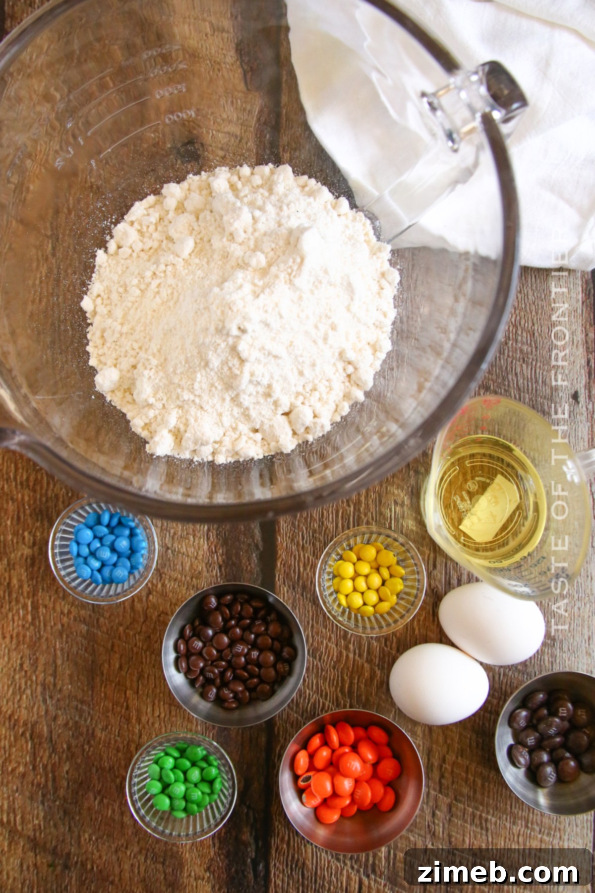 Festive Snowman Cookies 4 Simple ingredients laid out for making Snowman Cake Mix Cookies: white cake mix, cooking oil, eggs, and M&Ms.