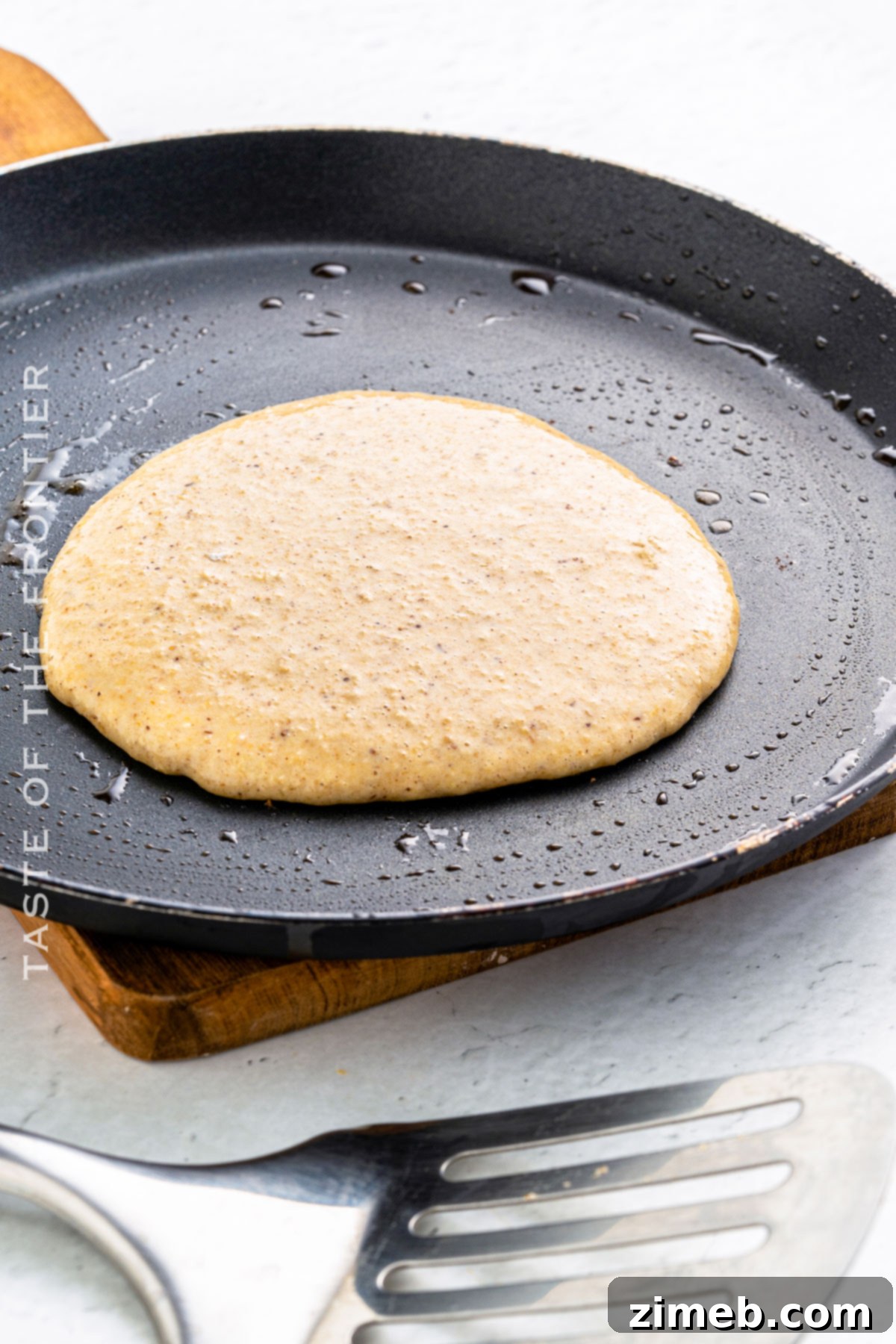 Wholesome Oat Pancakes 6 A hand pouring oat flour pancake batter onto a hot griddle, showing the cooking process.