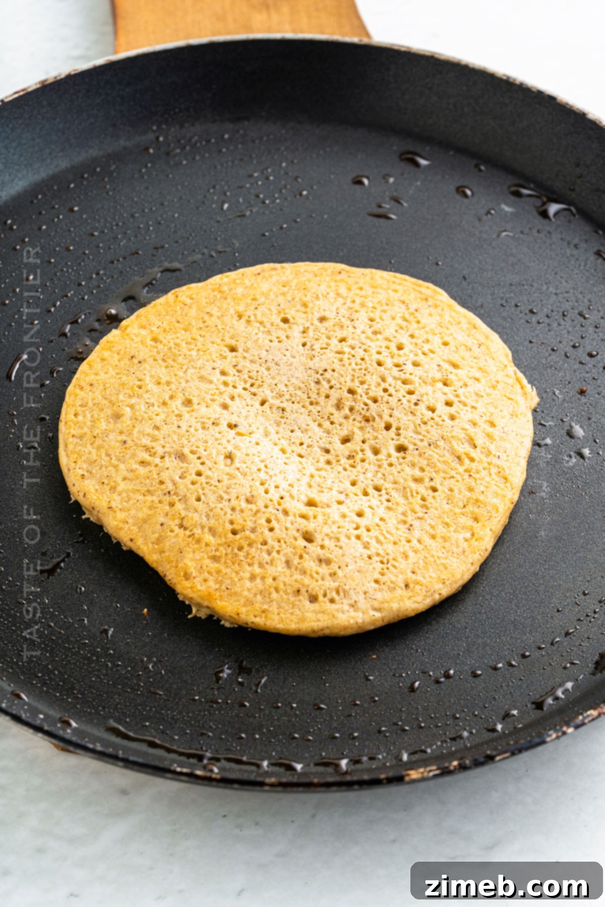 Wholesome Oat Pancakes 7 A close-up of a golden oat flour pancake cooking on a griddle, showing bubbles forming on the surface.