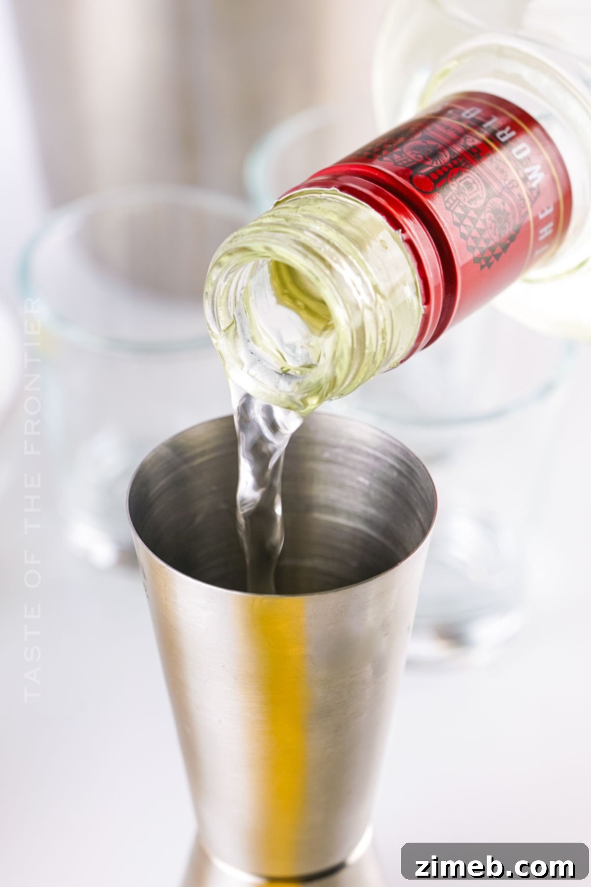 A bartender pouring vodka into a cocktail shaker, beginning the process of mixing Lemon Drop Shots.