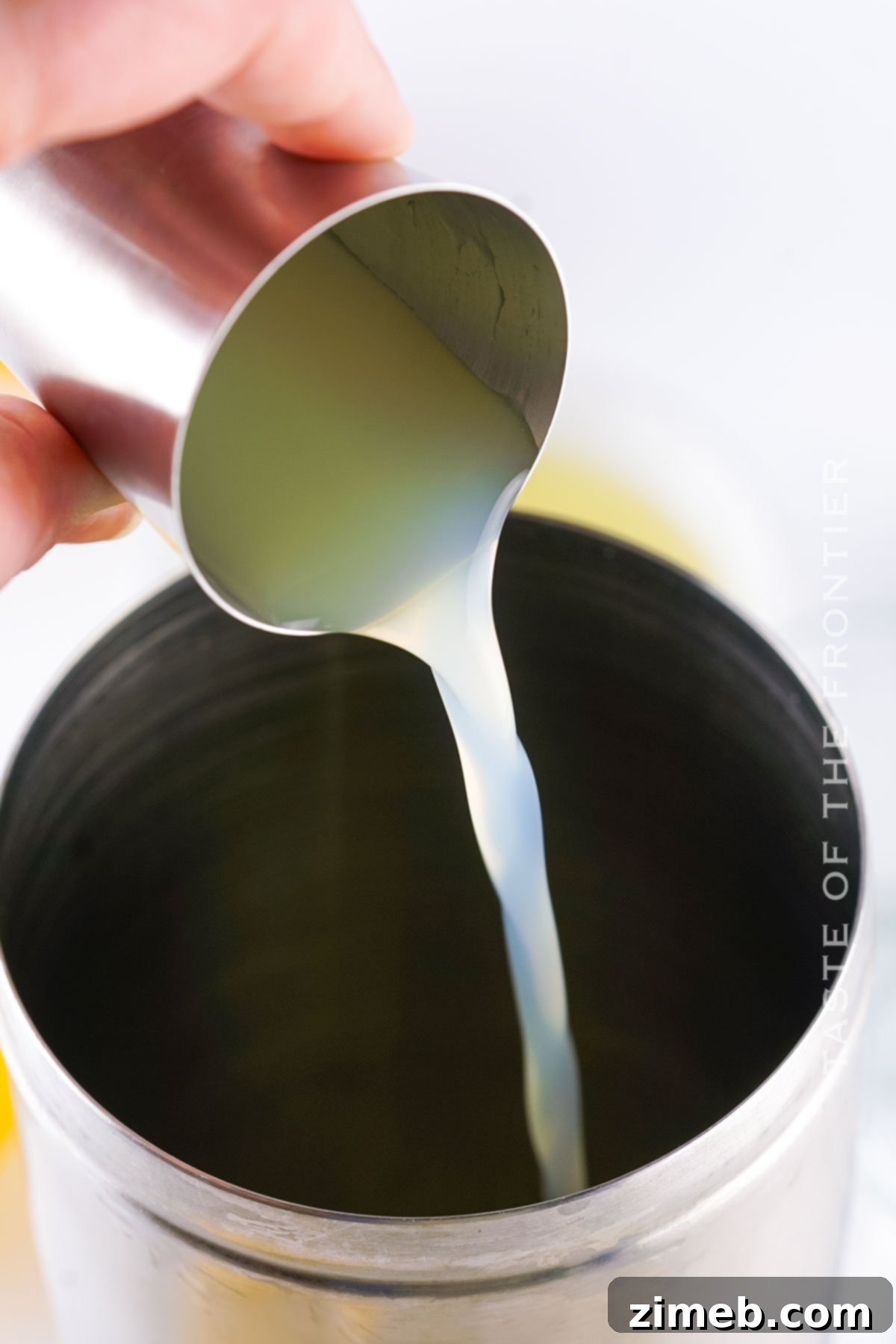 A hand placing a lemon wedge garnish on a freshly poured Lemon Drop Shot, completing the presentation.