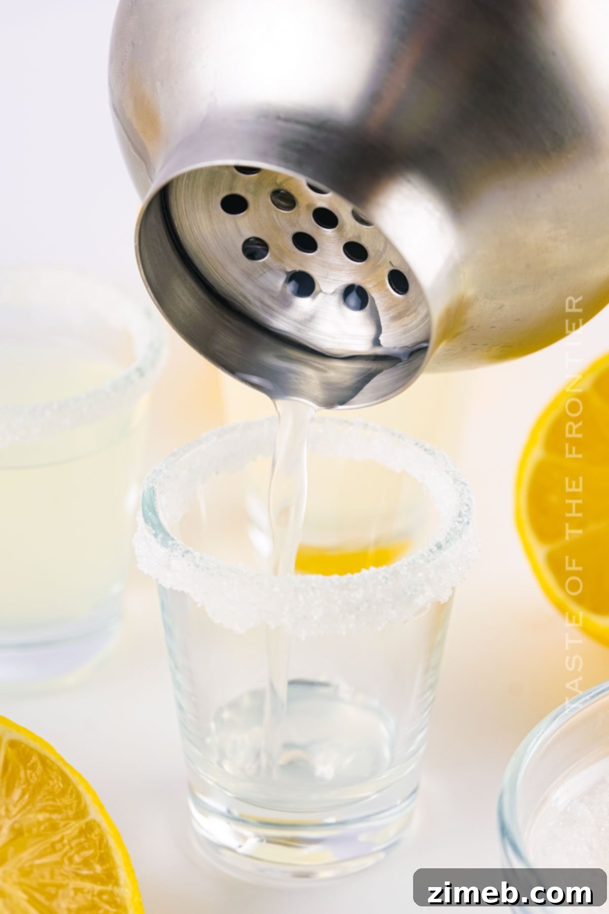 A close-up shot of a cocktail shaker being strained, pouring the mixed Lemon Drop Shots into glasses.