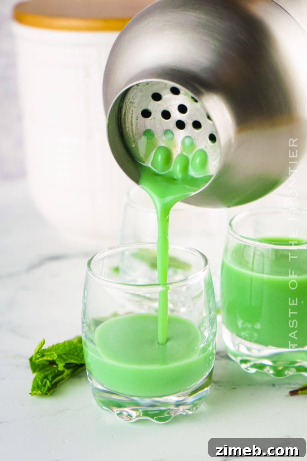Midnight Thin Mint Shooters 8 Three Dirty Girl Scout Shots lined up, showcasing the rich green color, with a shaker and ingredients in the background.