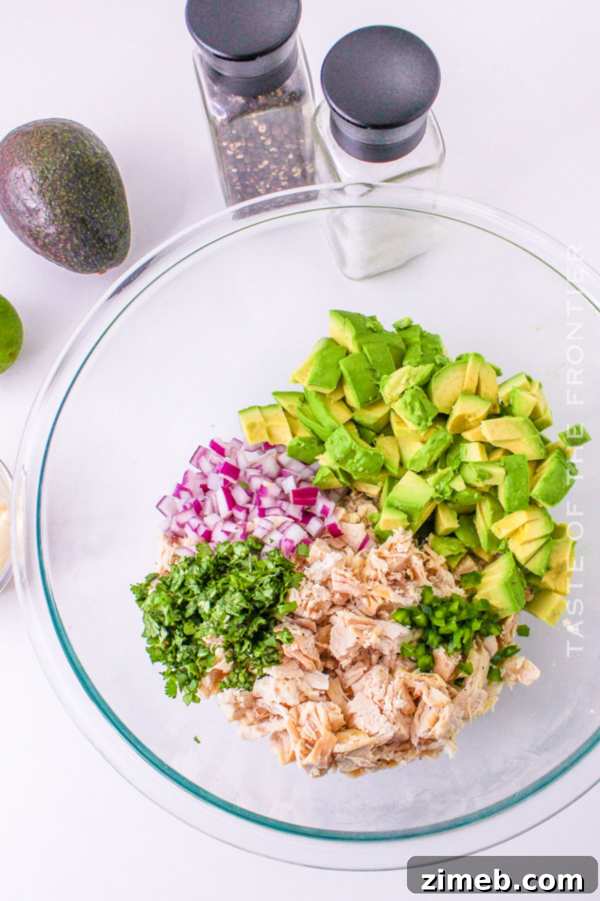 Easy Creamy Avocado Chicken Salad 5 A person mixing cold chicken salad with mayonnaise and fresh ingredients in a large bowl.