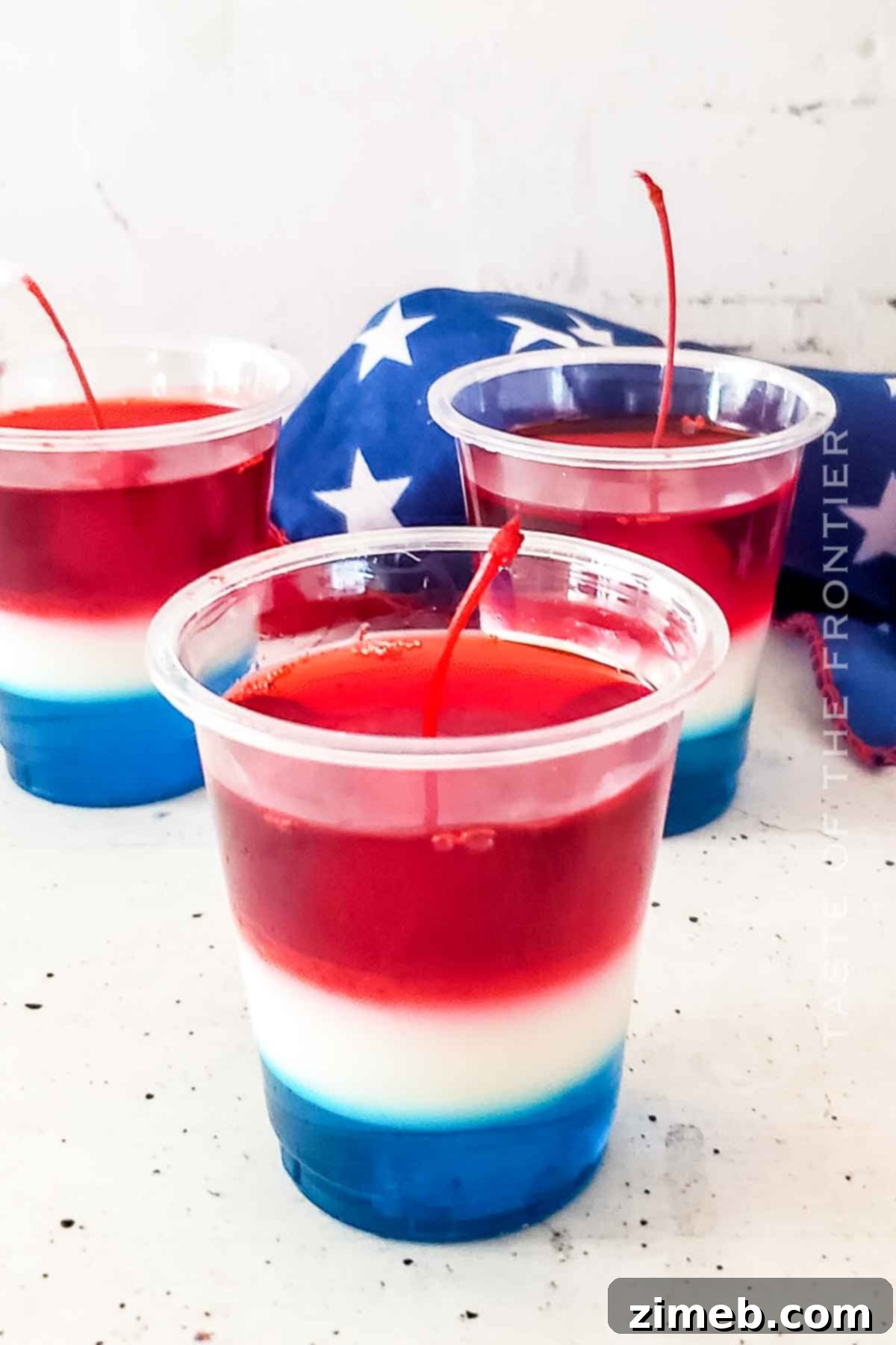 A close-up of the Bomb Pop Jello Shot recipe card with finished jello shots in the background.