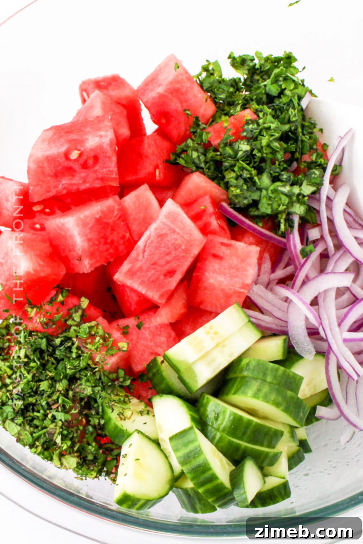 Someone gently mixing the watermelon salad ingredients in a large bowl.