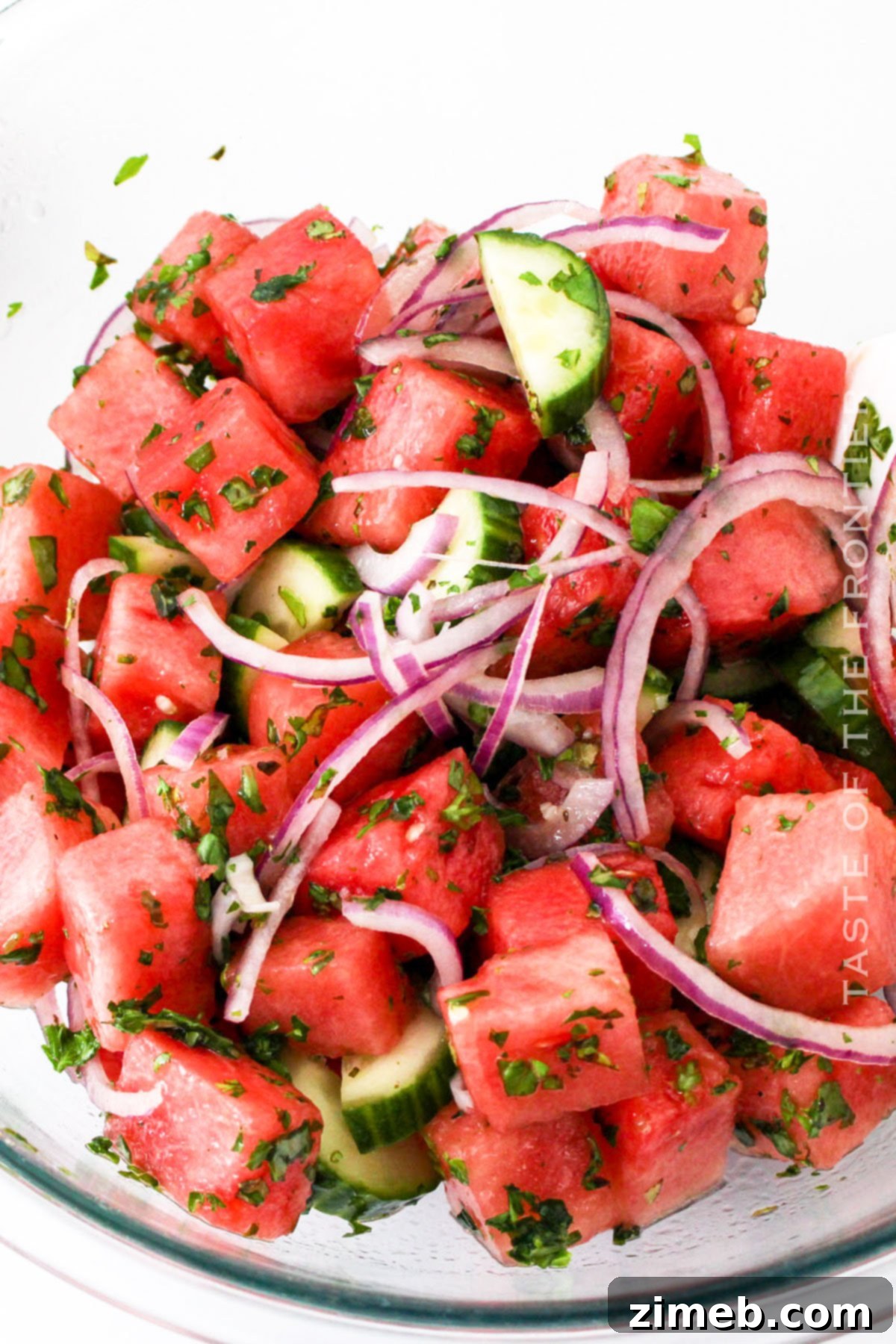 A close-up of the watermelon salad ingredients being gently tossed in a bowl.