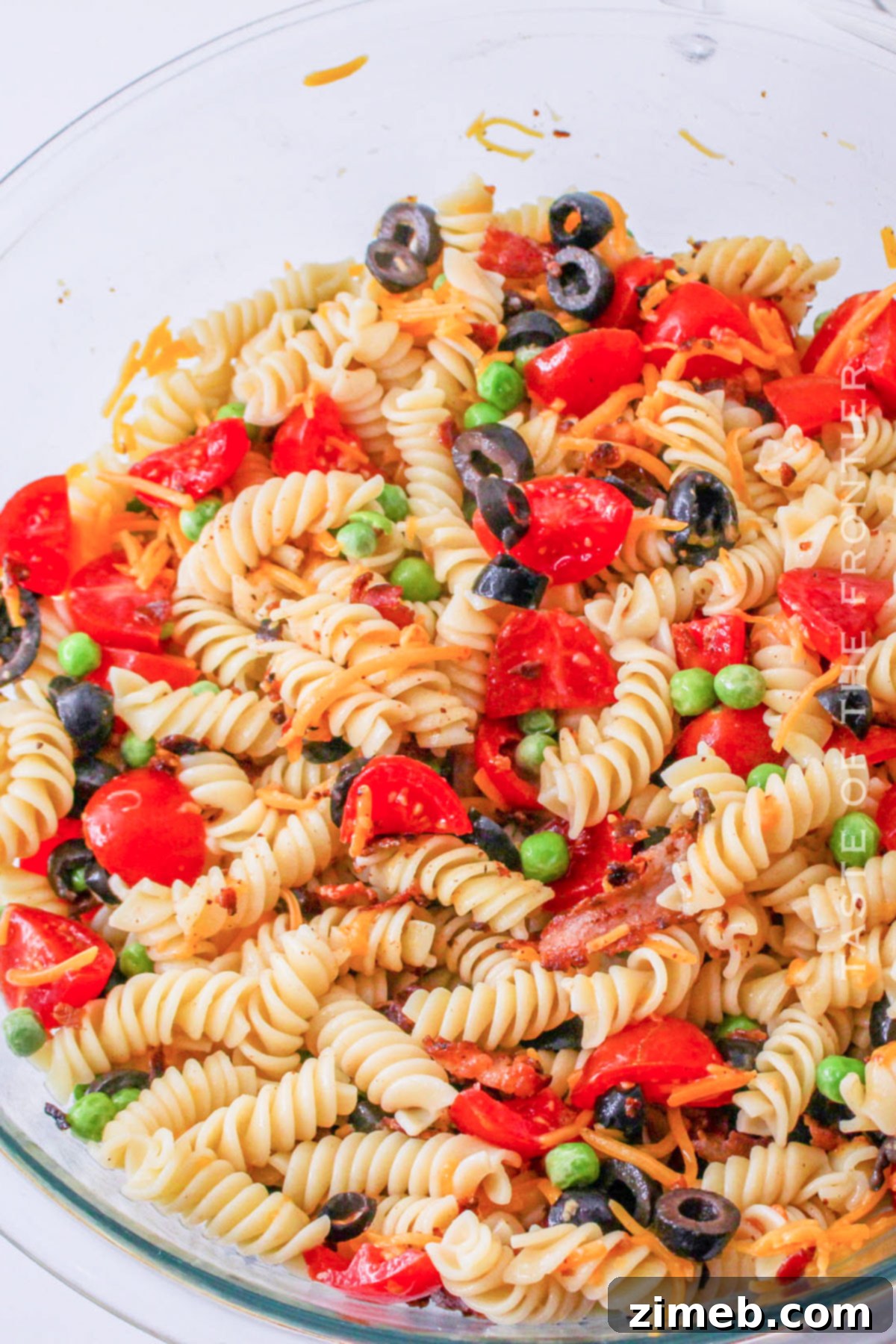 A large serving bowl filled with thoroughly tossed Bacon Ranch Pasta Salad, ready to be chilled.