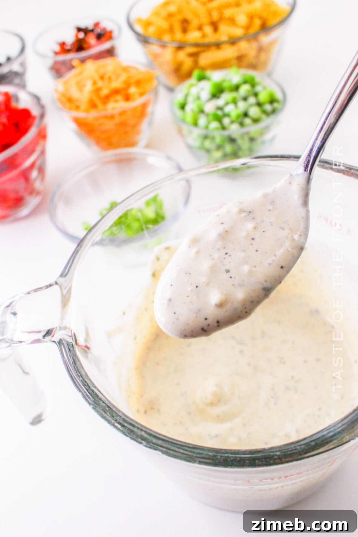 Close-up of the creamy ranch dressing being poured over the pasta salad ingredients.