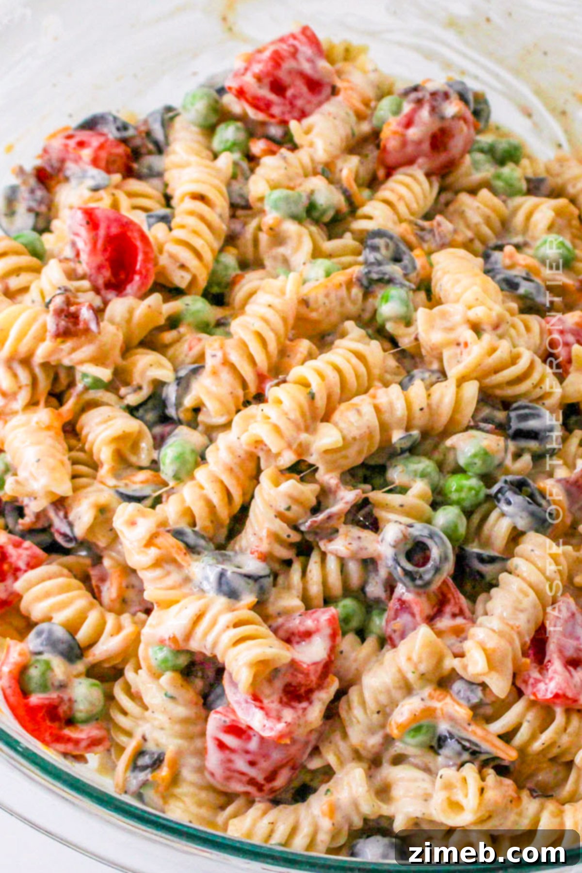 A hand mixing Bacon Ranch Pasta Salad in a glass bowl.