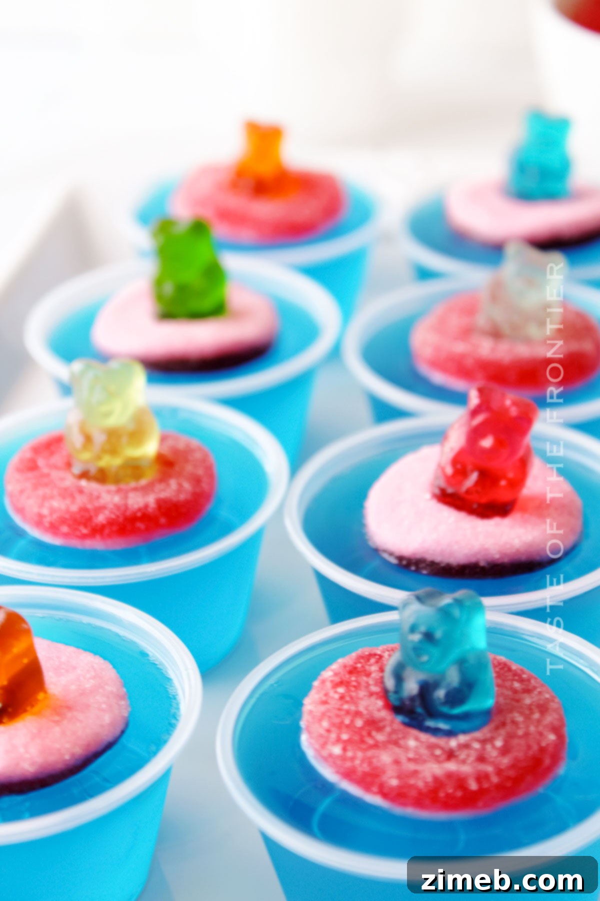 Assembling Pool Party Jello Shots with gummy bears and rings in clear cups.