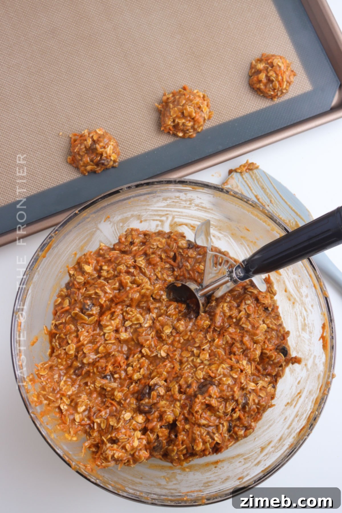 Hand scooping Carrot Cake Cookie dough onto a parchment-lined baking sheet