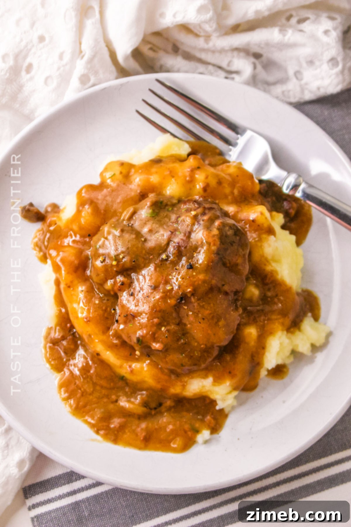 Tender Slow Cooker Cube Steak 12 Onion Soup Gravy with Beef - Rich, thick gravy covering tender beef patties, ready to be served.