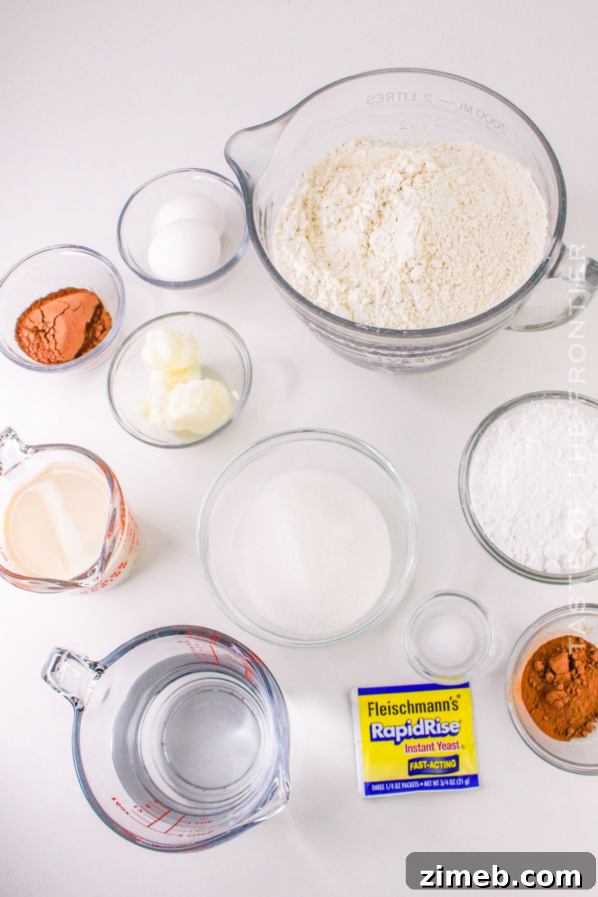 Ingredients for chocolate beignets laid out on a table, including flour, cocoa powder, sugar, and eggs