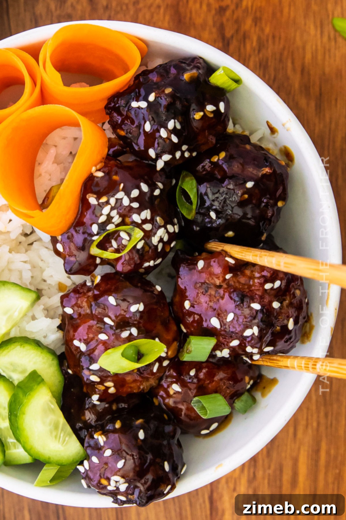Sticky Asian Pork Meatballs 3 A vibrant dinner plate featuring Asian Pork Meatballs, garnished with green onions and sesame seeds, alongside rice and steamed vegetables.