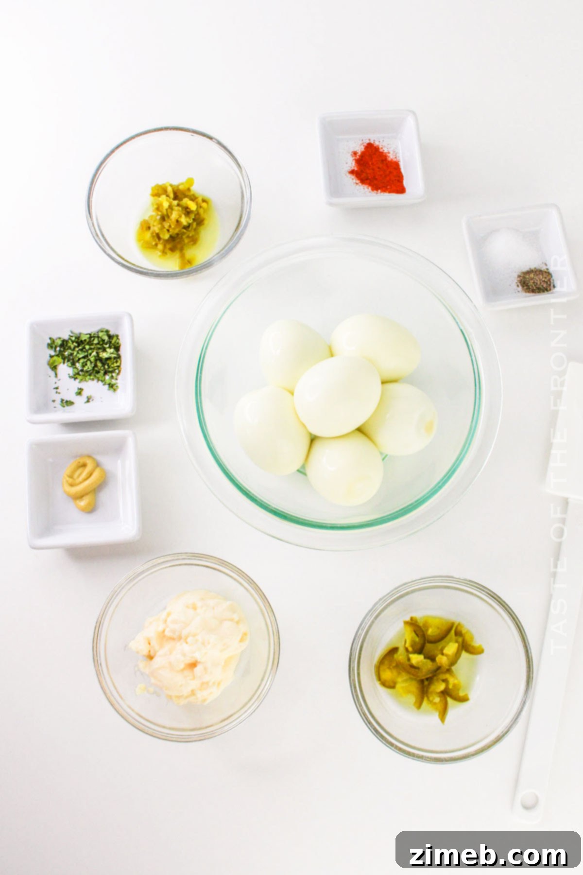 Zesty Jalapeño Deviled Eggs 4 Ingredients for Jalapeno Deviled Eggs laid out on a white surface: hard-boiled eggs, mayonnaise, Dijon mustard, pickled jalapenos, salt, pepper, and paprika.