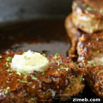 A perfectly cooked filet mignon drizzled with garlic butter, served on a white plate. The steak has a rich, seared exterior with a tender, juicy center. Fresh herbs and a drizzle of melted butter enhance the savory presentation, making it an elegant and mouthwatering meal, ideal for a special occasion like Valentine's dinner.