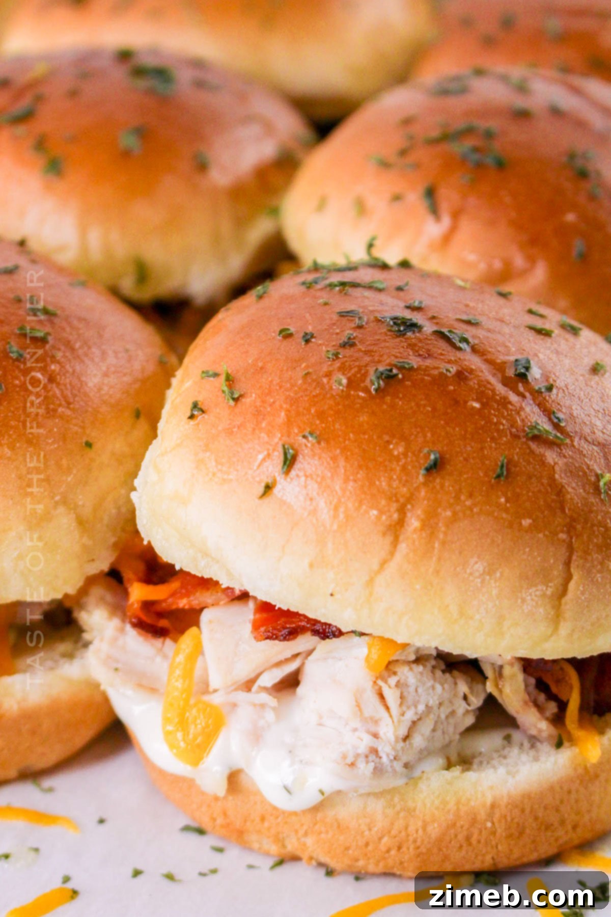 Ultimate Bacon Ranch Chicken Sliders 2 Bacon Chicken Ranch Sliders - a close-up shot of several sliders on a baking sheet, showcasing melted cheese, crispy bacon, and chicken nestled in soft buns.