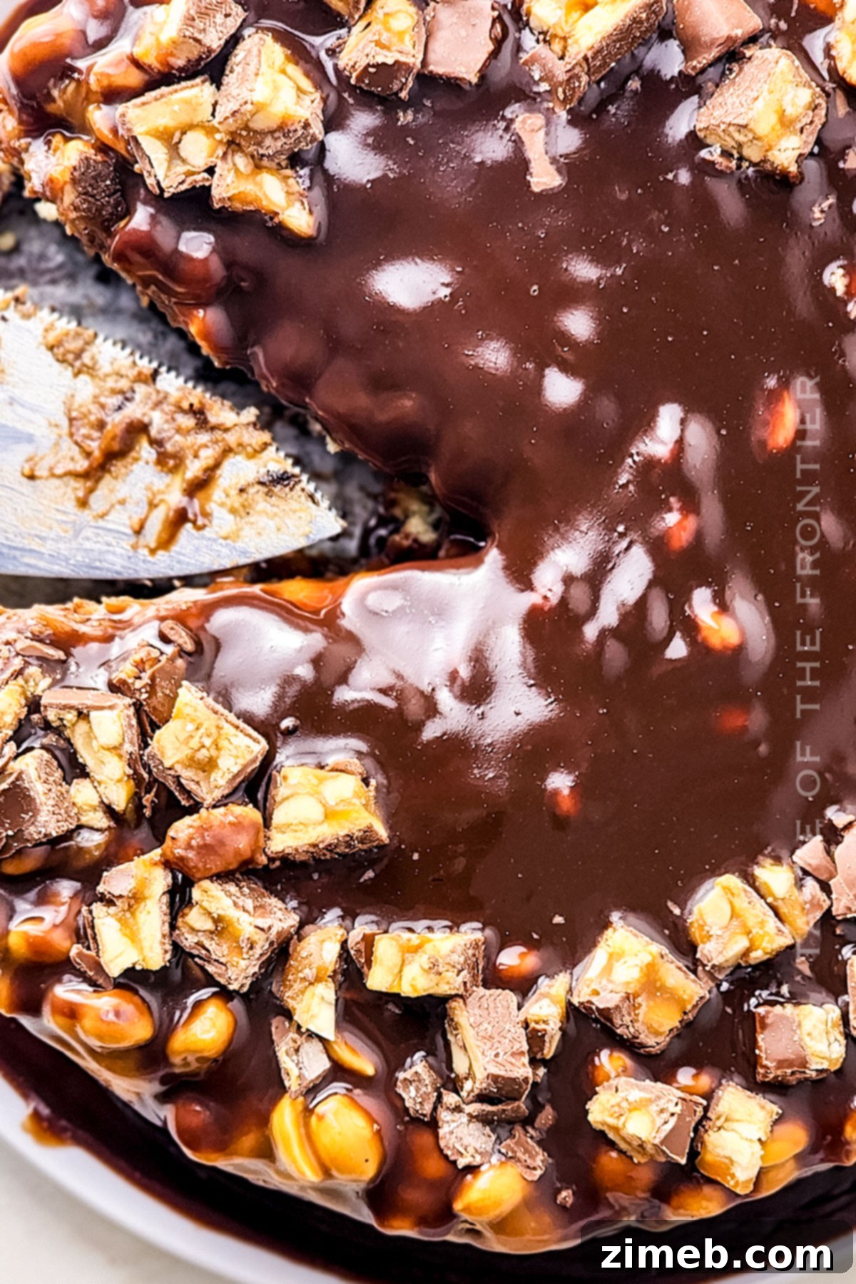 Close-up of a loaded Snickers Cheesecake with visible Snickers chunks, chocolate, and caramel layers.