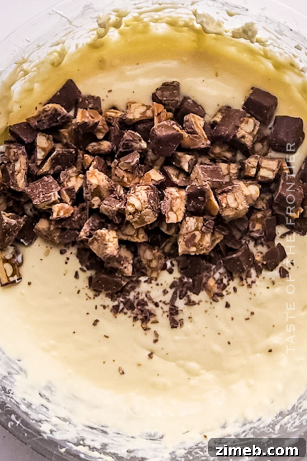 Chopped Snickers candy bars being folded into creamy cheesecake filling.
