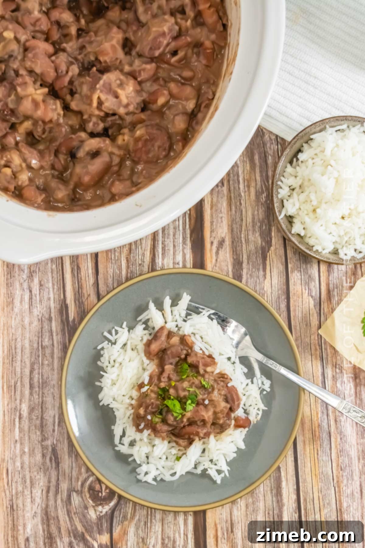 A vibrant bowl of Crockpot Red Beans & Rice, served with fresh parsley and a side of fluffy white rice.