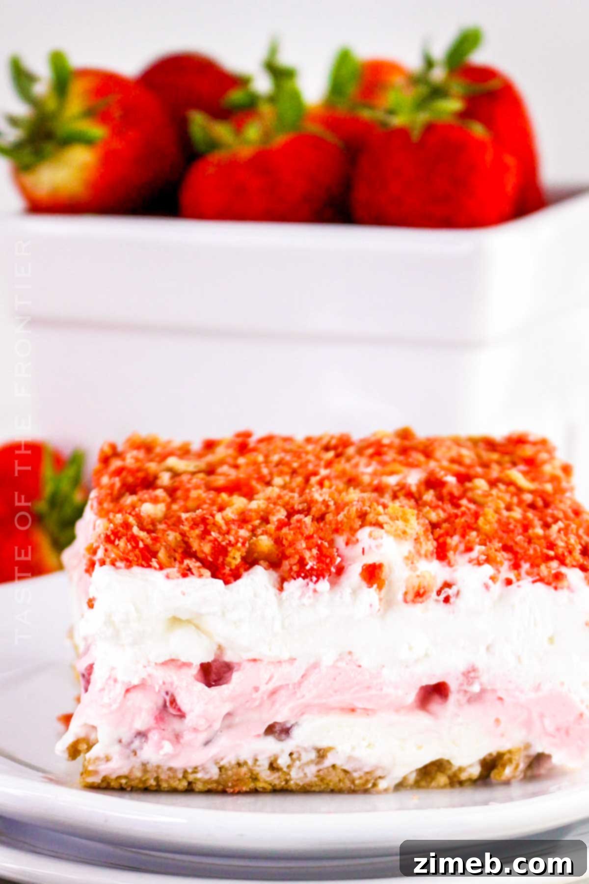 Crimson Indulgence 3 Close-up of a slice of No-Bake Strawberry Delight, showing distinct layers of whipped topping, strawberry cream cheese, sliced strawberries, and a graham cracker crust.