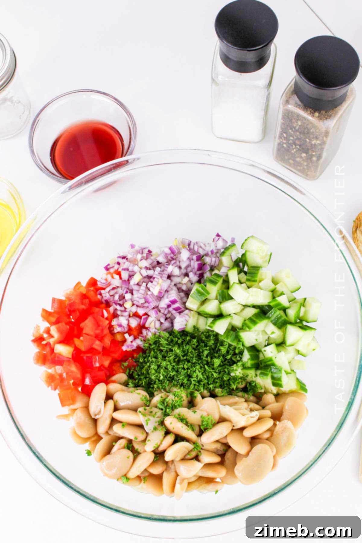 Hands gently tossing Butter Bean Salad in a large mixing bowl.