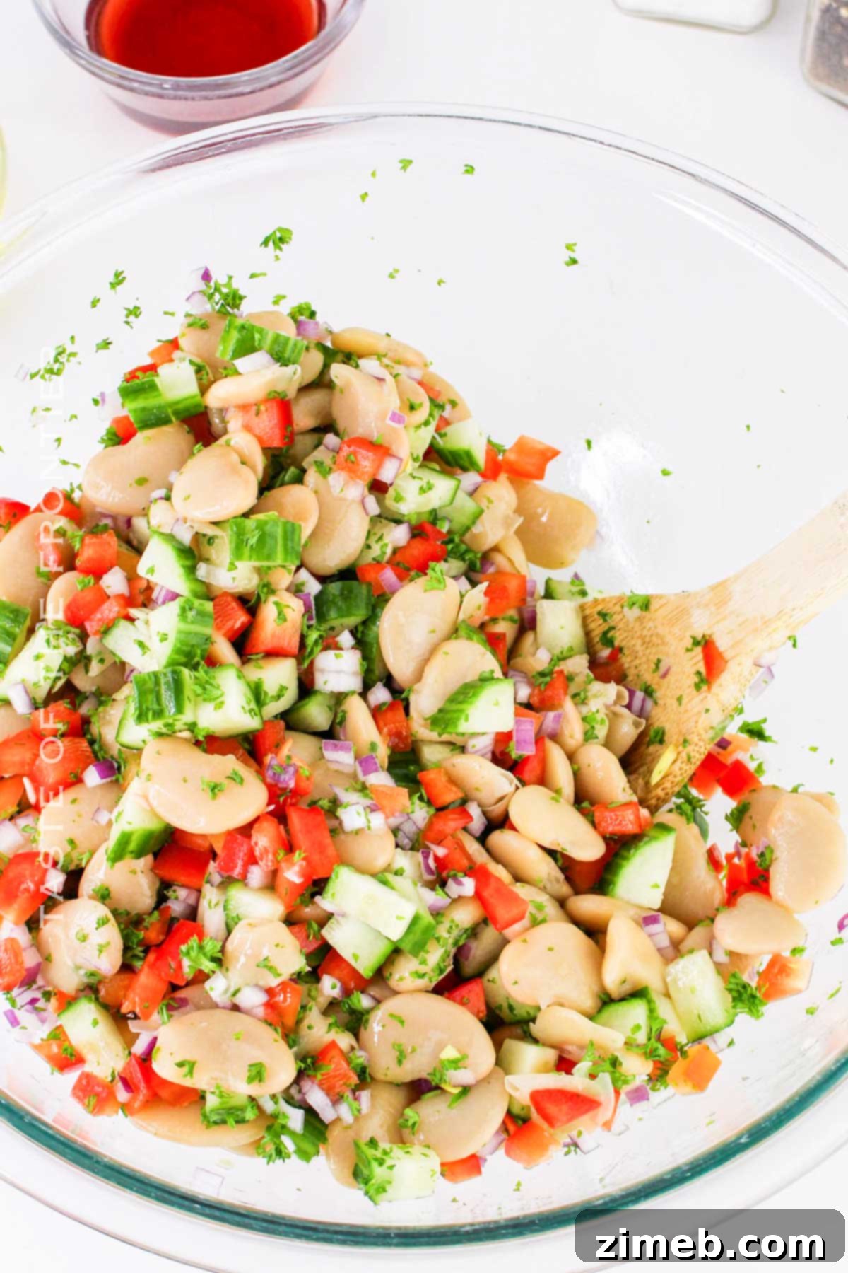A large bowl of Butter Bean Salad being tossed gently with dressing, showcasing fresh ingredients.