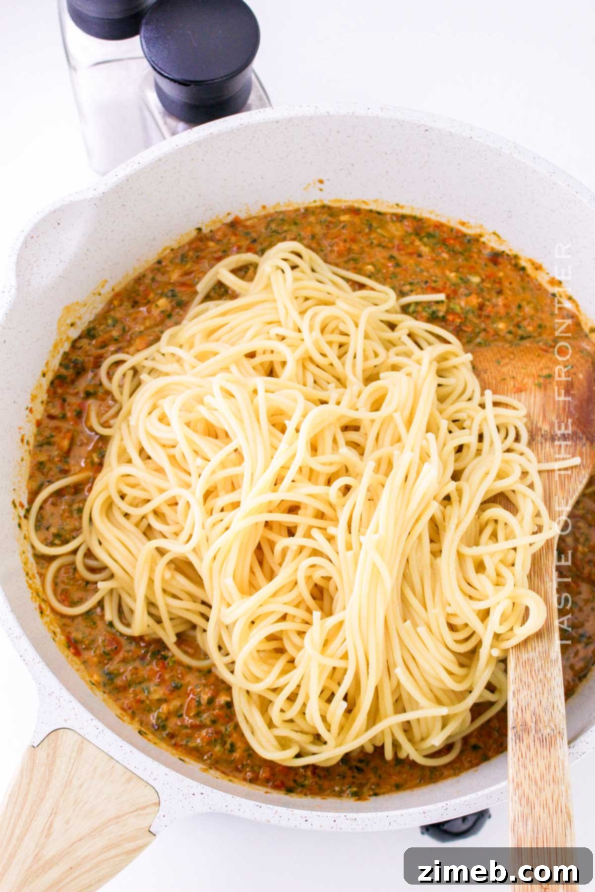 Sicily's Sun-Kissed Tomato Pesto 8 Spaghetti noodles being added to the Pesto alla Trapanese sauce in a skillet