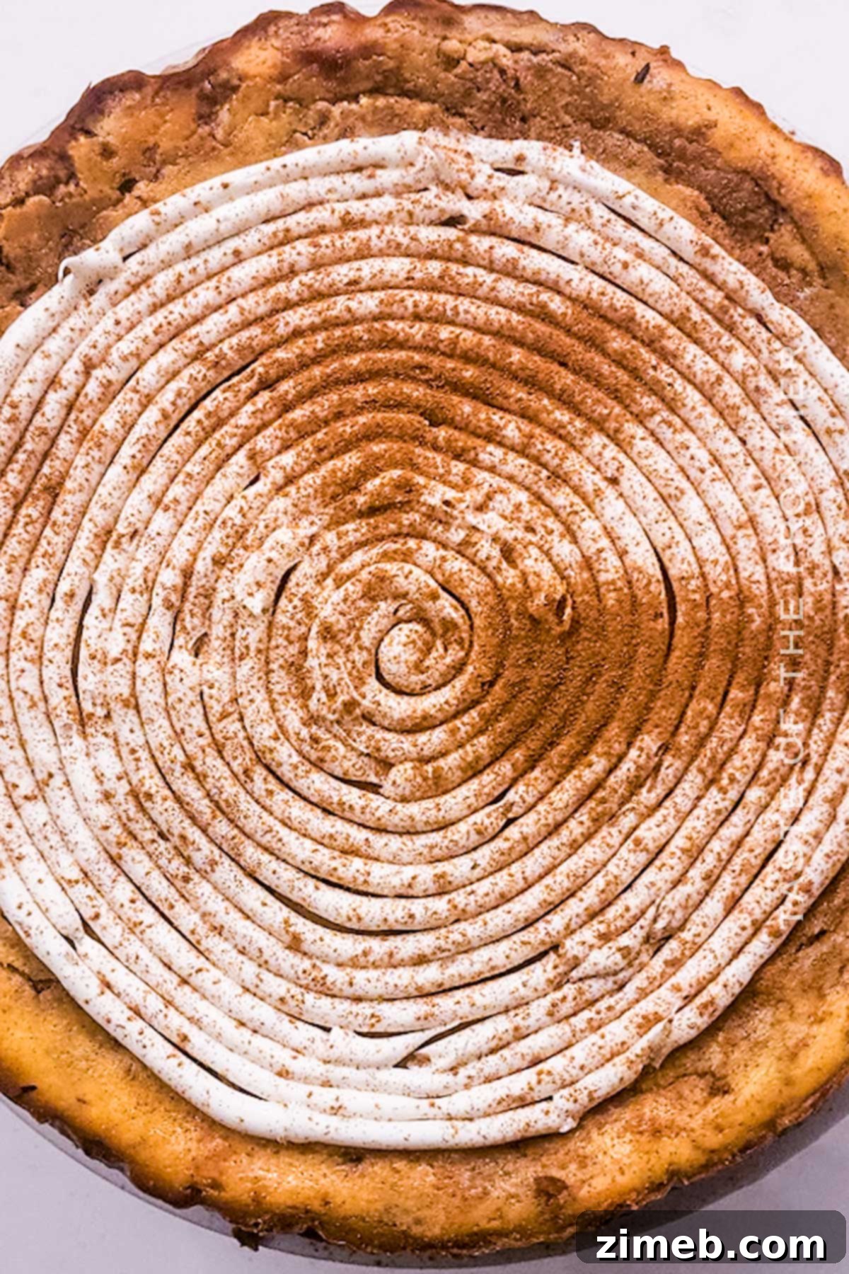 Cream cheese frosting being swirled on top of a cheesecake
