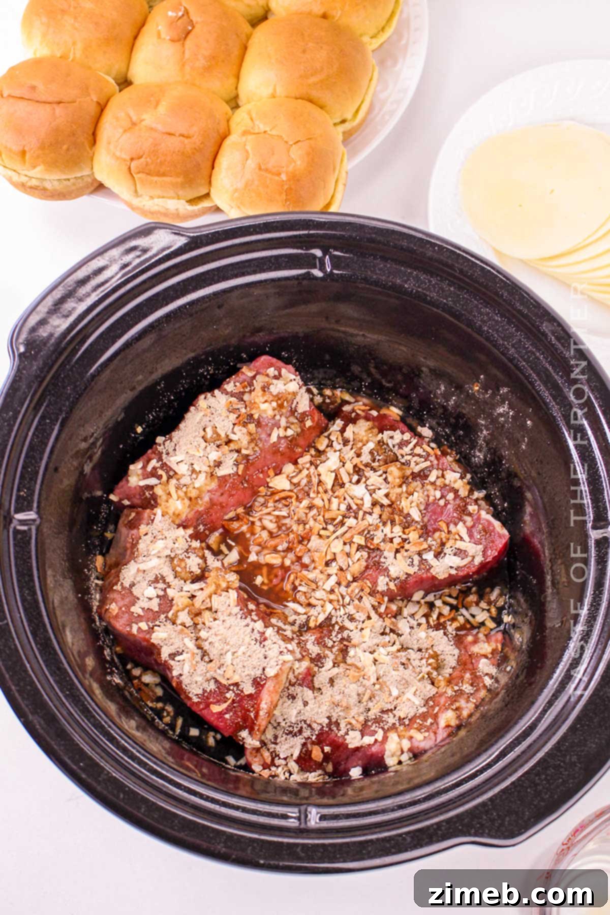 A hand placing a slider bun top onto assembled beef and cheese
