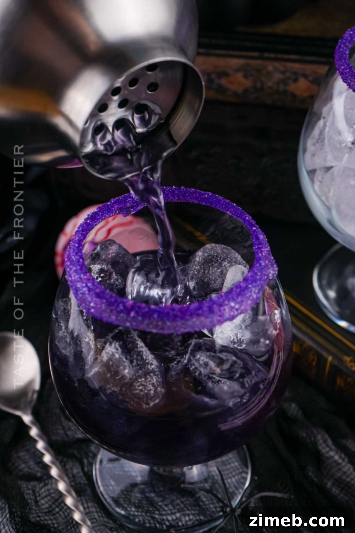 Cocktail shaker pouring a purple drink into a glass