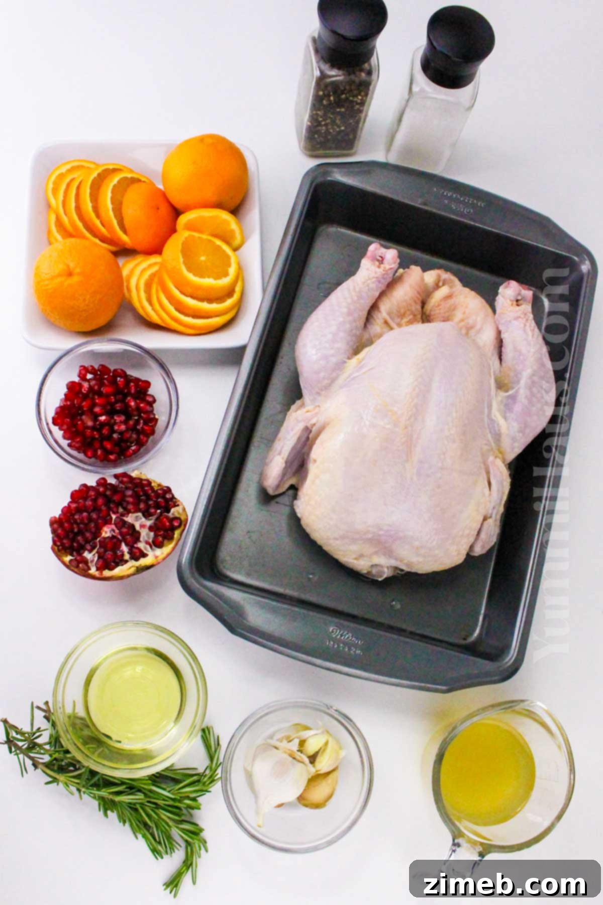 The Yuletide Bird 4 Christmas Chicken ingredients laid out for preparation, featuring a whole chicken, oranges, rosemary, garlic, and cranberries.