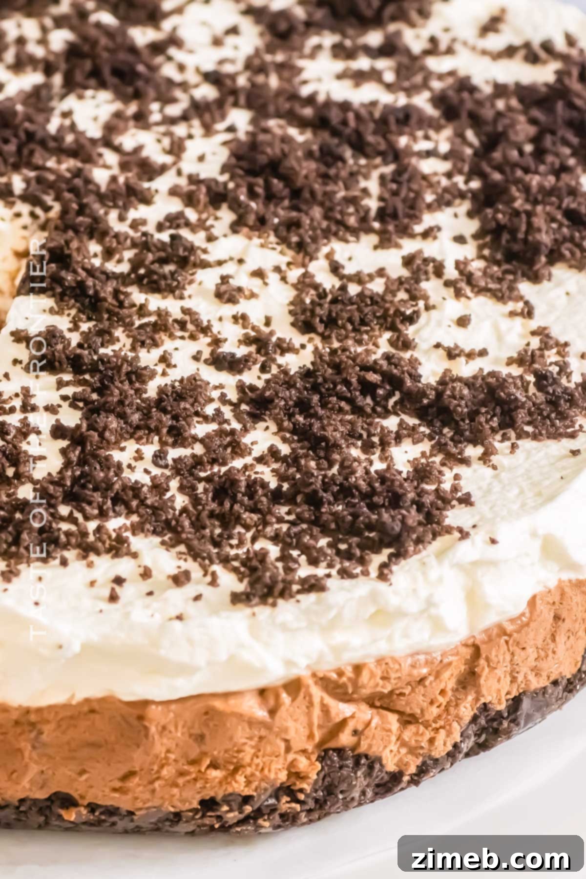 Decadent Oreo Mousse Cake 3 Layered dessert showing Oreo crust, chocolate mousse, and whipped cream with crushed Oreos on top.