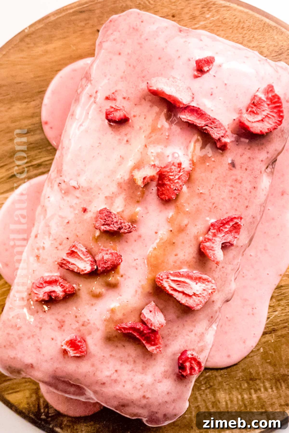 Close-up of pink glaze being poured over a sweet bread, with fresh strawberries for garnish.