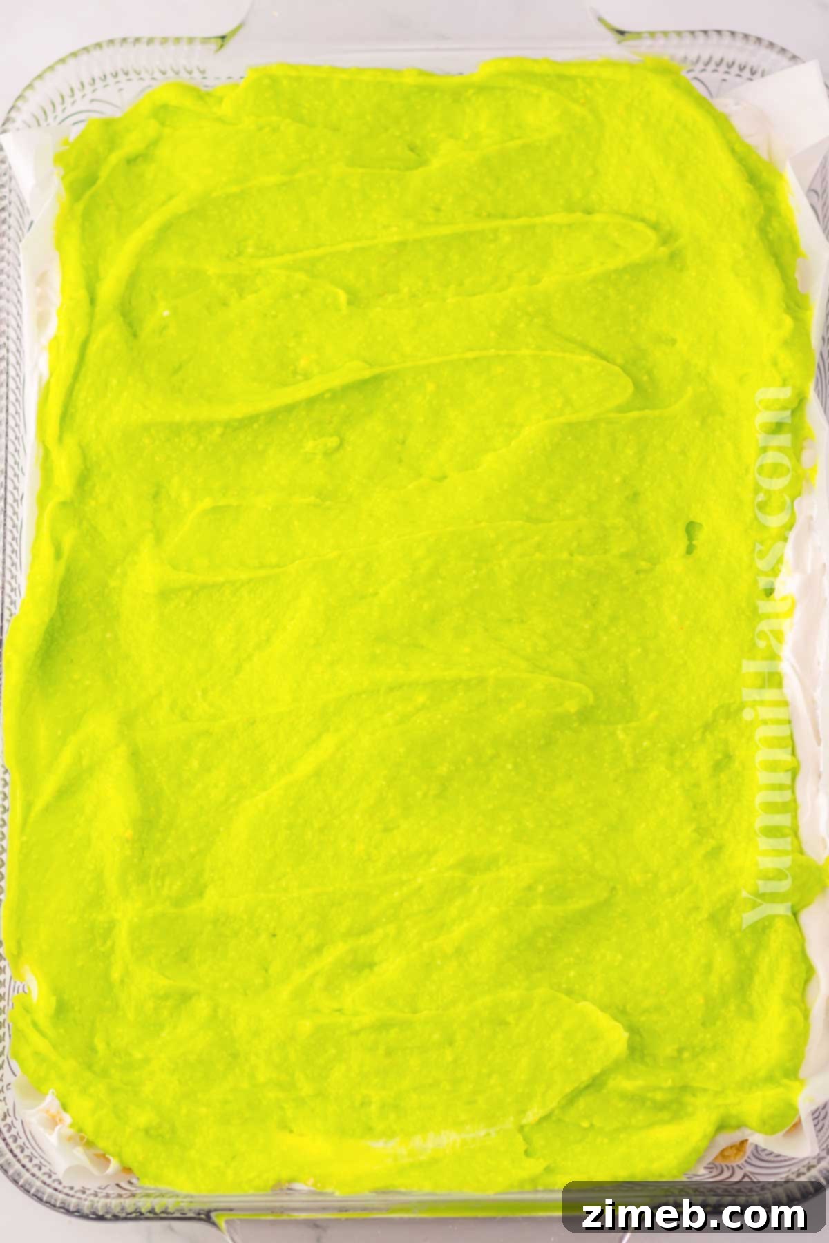 Rainbow Charm Elixir 7 Close-up of the vibrant green cream cheese layer being spread over the Oreo crust in a baking dish