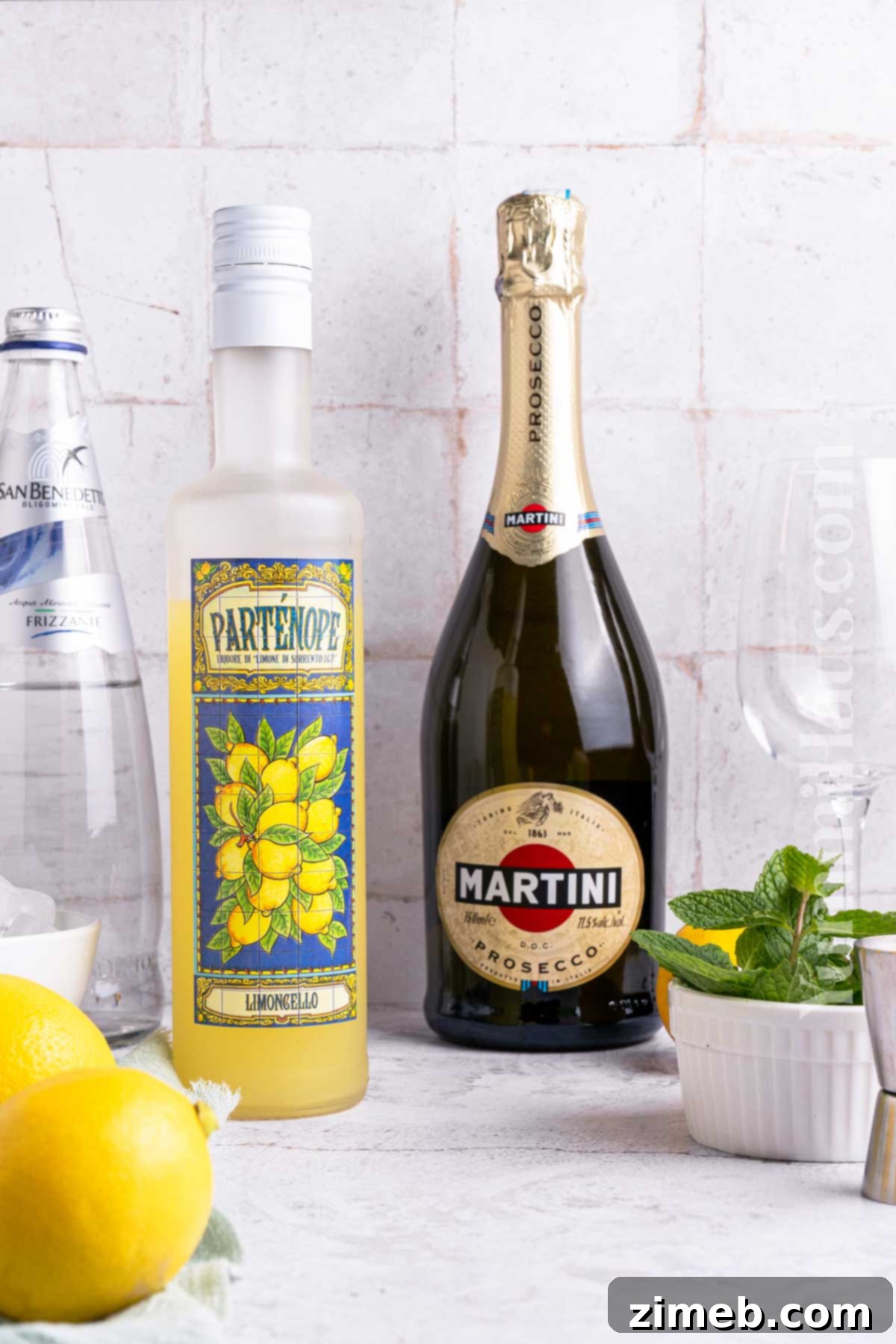 Refreshing Limoncello Spritz 4 Fresh ingredients for a Limoncello Spritz laid out on a table, including limoncello, prosecco, and lemons