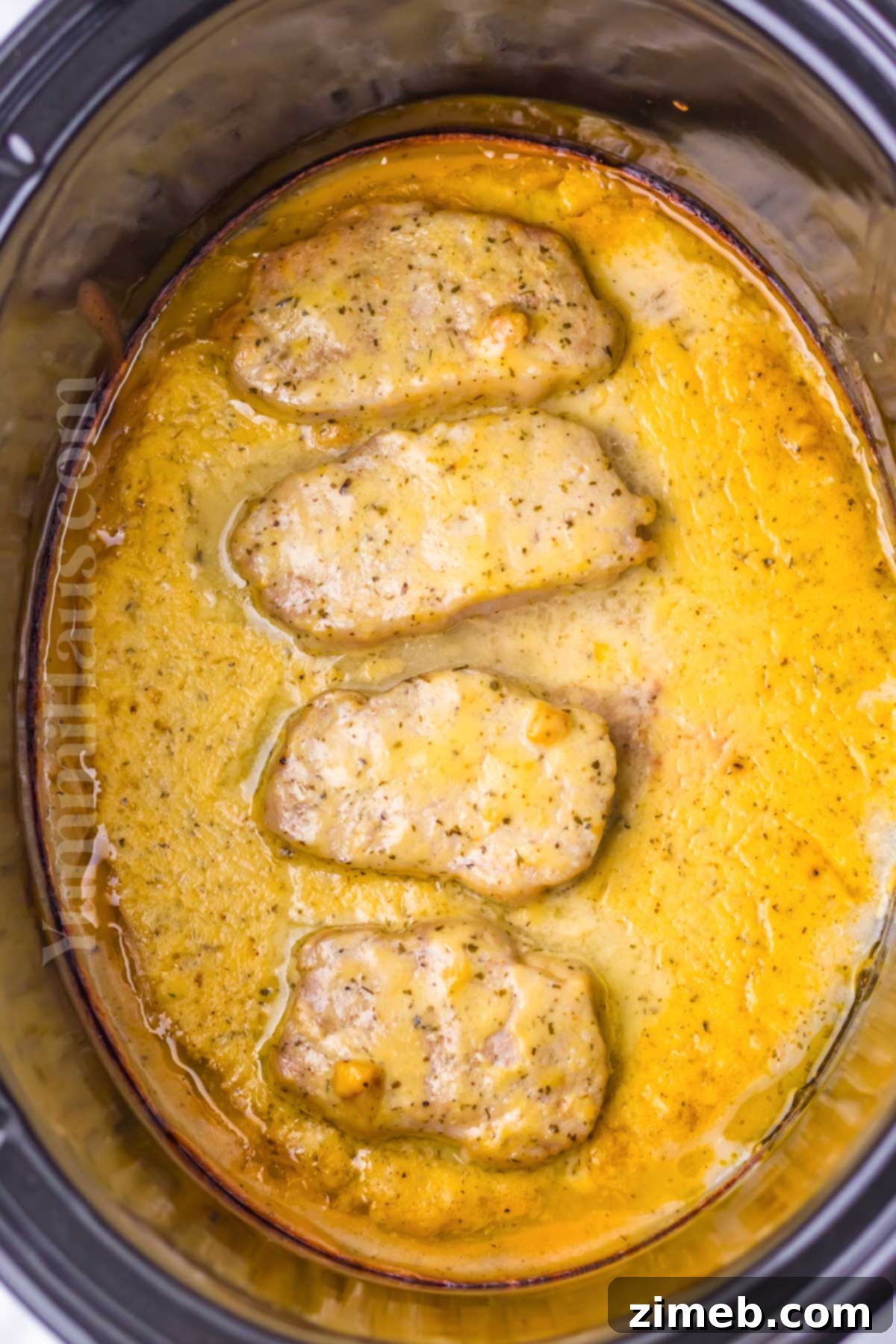 Cooked ranch pork chops in the crockpot, simmering in creamy gravy.