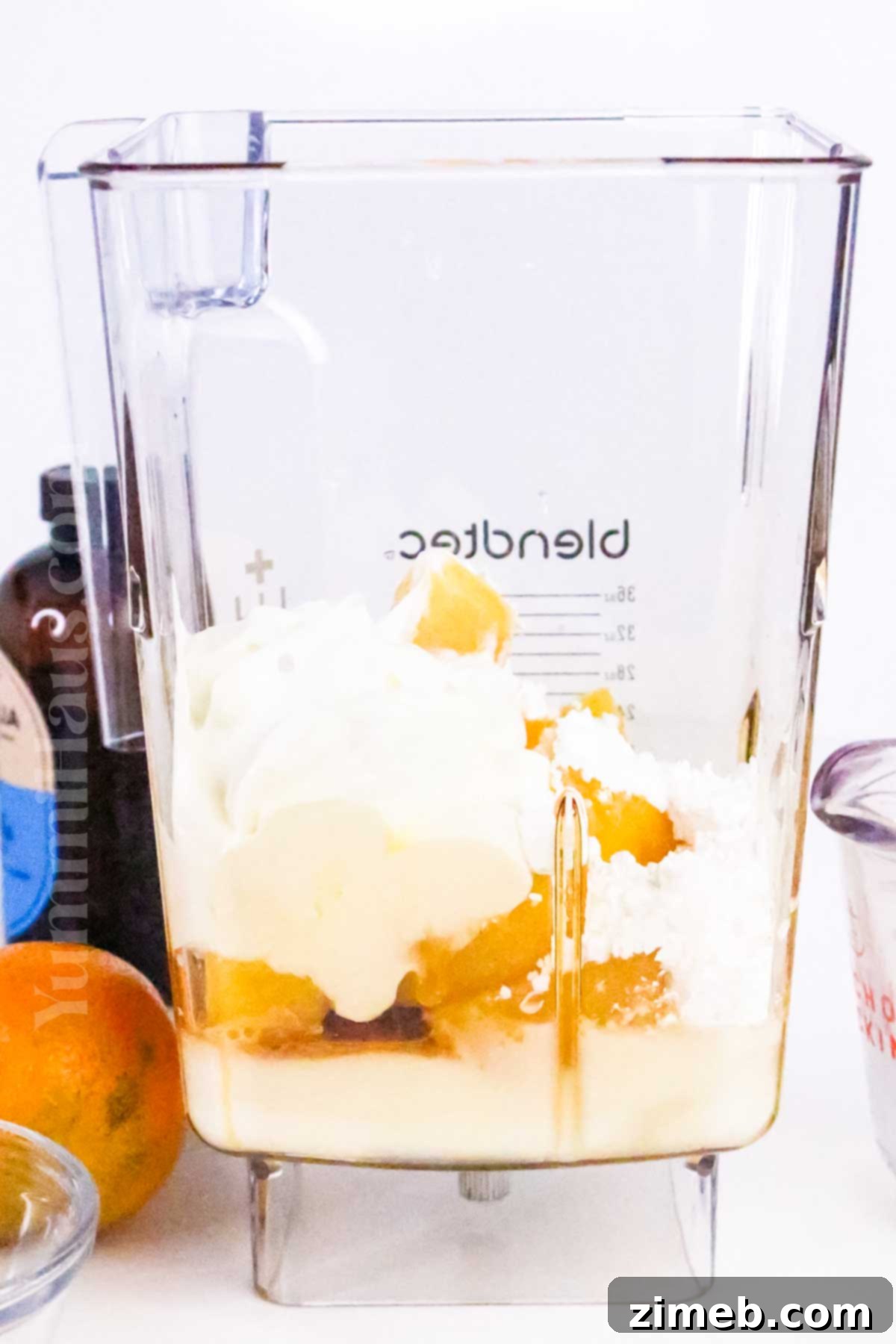 Close-up of a blender filled with all ingredients for a homemade Orange Julius, ready to blend