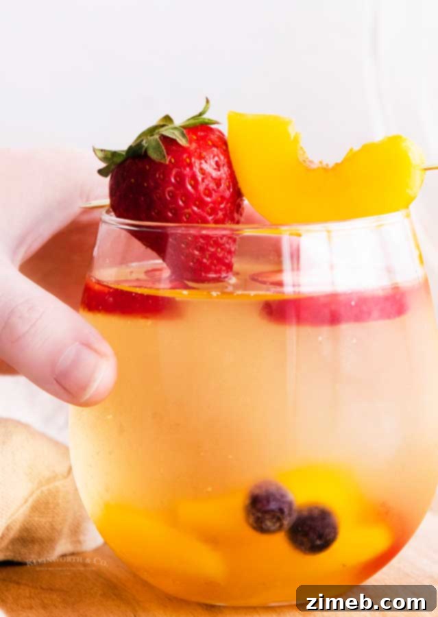 A refreshing glass of White Peach Sangria, filled with slices of fresh peaches and other fruits, perfect for a summer celebration.