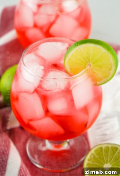 A tall glass of Dirty Shirley cocktail with ice, garnished with a maraschino cherry and a lime wedge, against a bright background.