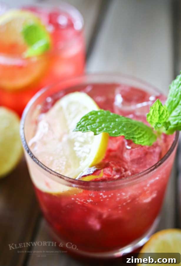 A tall glass of Blackberry Lemon Gin & Tonic, featuring a vibrant purple hue, garnished with fresh blackberries and lemon slices, with ice.