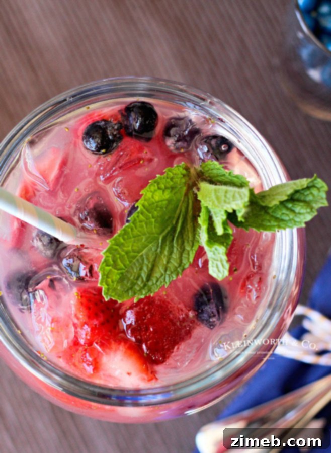 A layered Red, White & Blue Daiquiri in a hurricane glass, showing distinct red, white, and blue sections, garnished with fruit.