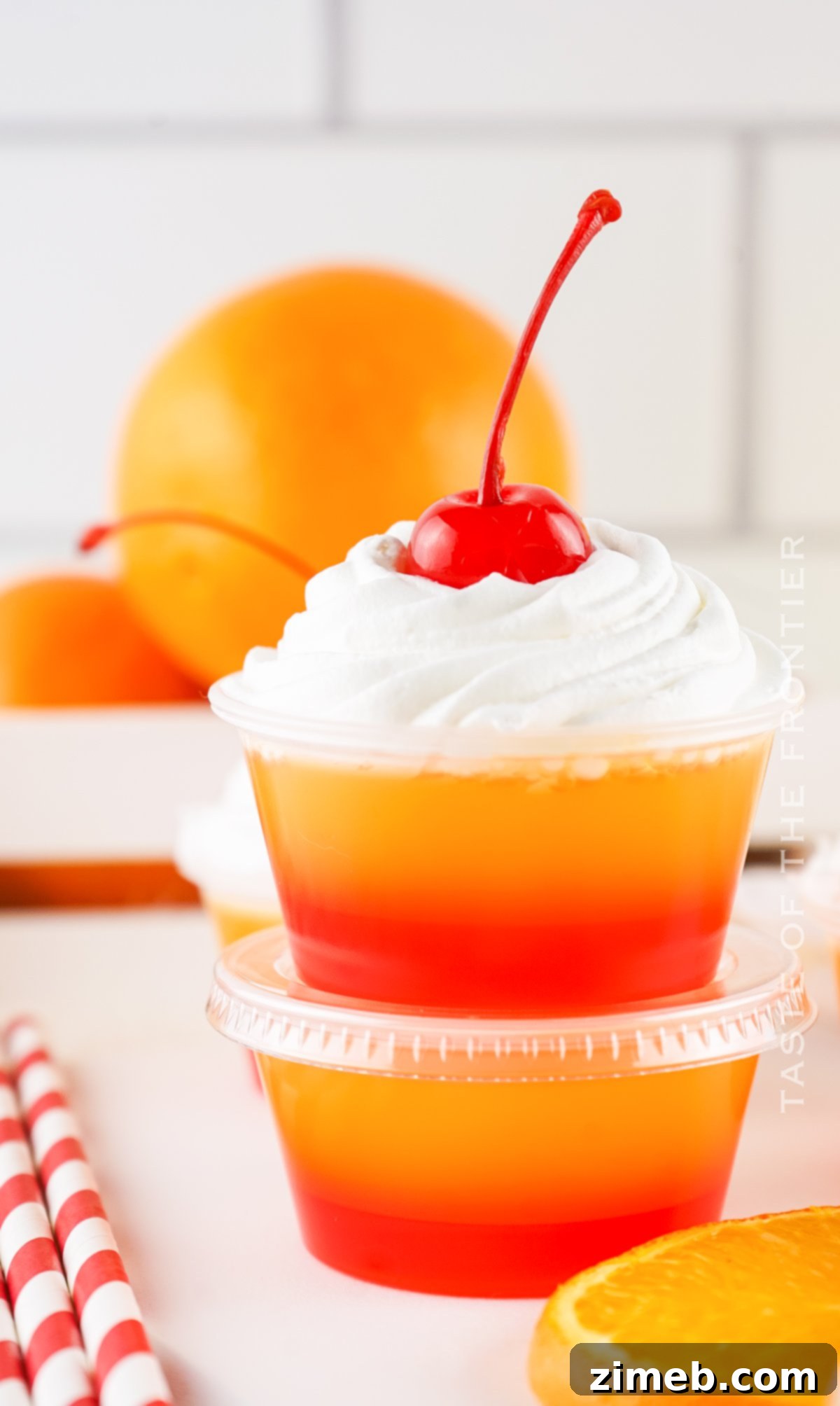A collection of Tequila Sunrise Jello Shots in clear cups, showing the gradient of red to orange, topped with whipped cream and a cherry.