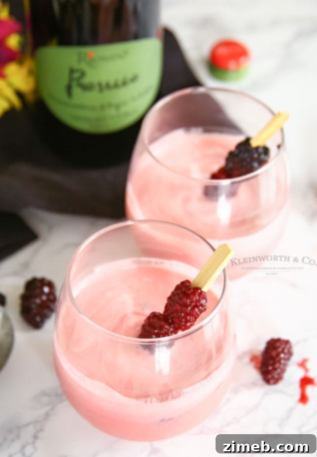A elegant Blackberry Cream Mimosa in a champagne flute, showing creamy white and purple layers, garnished with fresh blackberries.